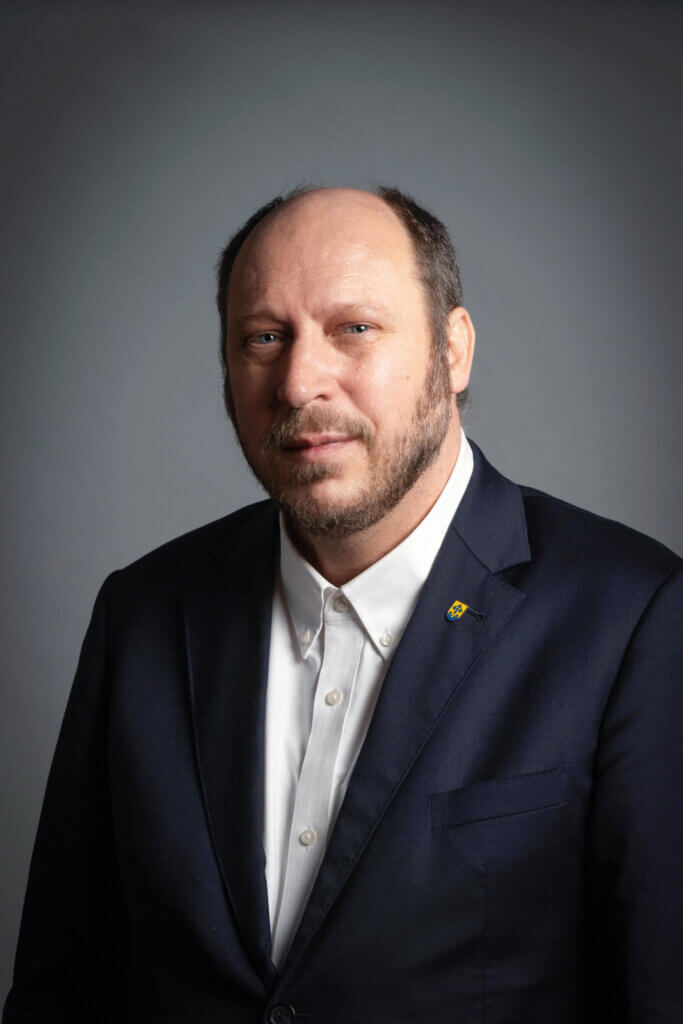 Porträt eines Mannes im Anzug vor grauem Hintergrund, passend zum professionellen Image von Prima Magazin.