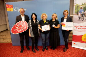Gruppe von fünf Menschen beim Event Burgenland radelt mit Urkunde und Plakaten, unterstützt von Land Burgenland.