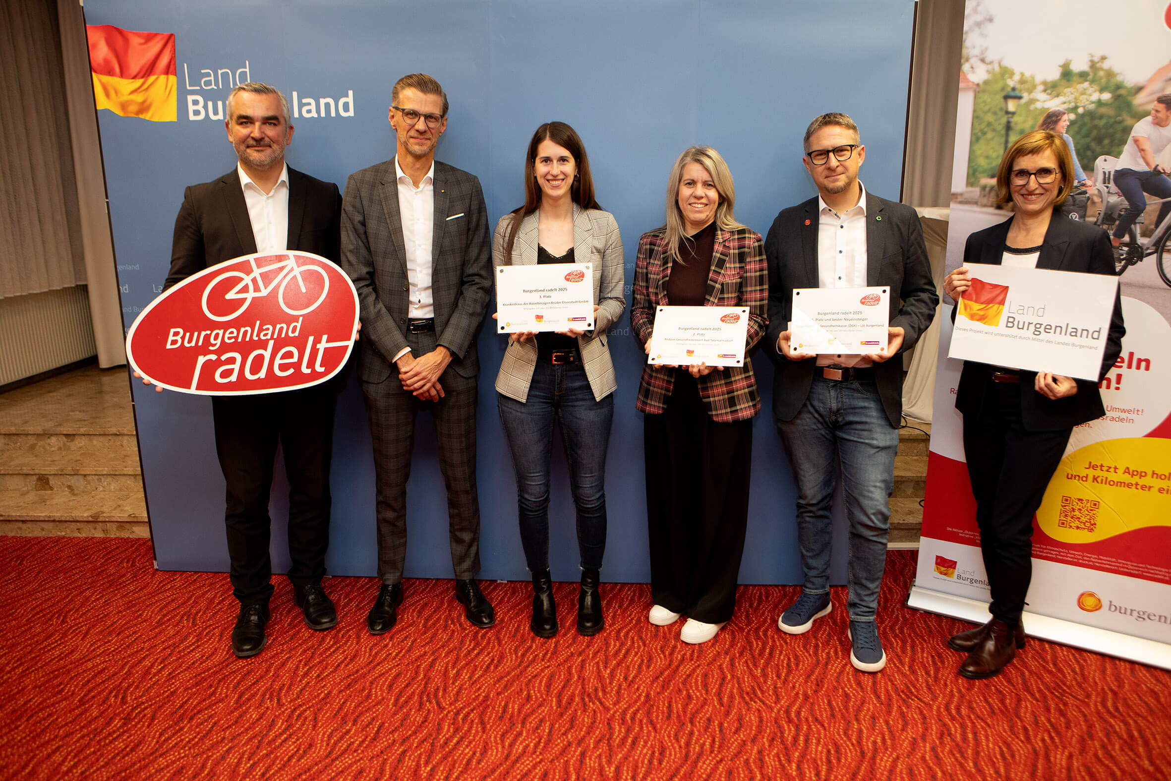 Menschen bei einem Event im Burgenland, halten Schilder der Aktion „Burgenland radelt“ und Urkunden stolz in den Händen.