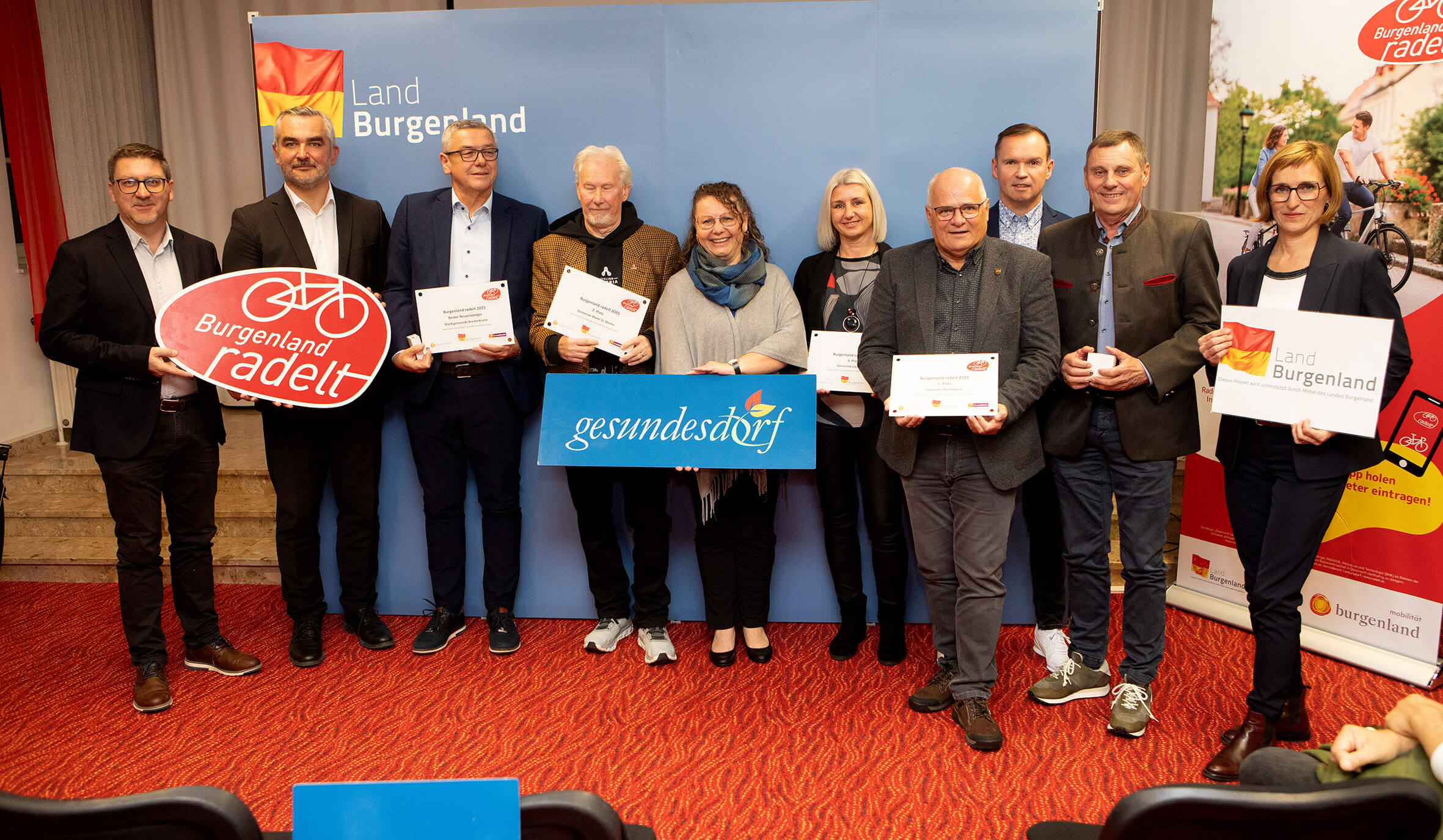 Gruppe lächelnder Personen beim Burgenland radelt-Event, präsentieren Auszeichnungen und Banner in festlichem Rahmen.