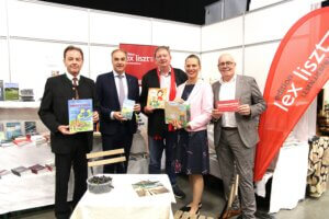Gruppe von fünf Personen steht vor einem Buchstand, hält Bücher in den Händen und lächelt in die Kamera, bei einer Buchmesse.