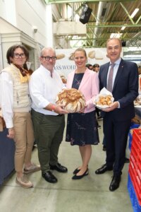 Gruppe präsentiert regionales Brot und Gebäck auf Messe, symbolisiert Engagement für lokale Backkunst und Qualitätsjournalismus.