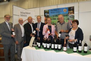 Gruppe von Personen präsentiert Weine auf einer Messe am Stand von Wachter Wein. Ideal für Prima Magazin über regionale Weinkultur.