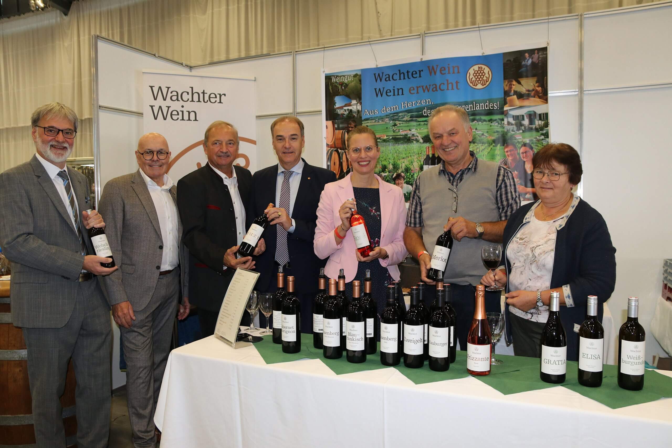 Gruppe von Personen präsentiert Weine auf einer Messe am Stand von Wachter Wein. Ideal für Prima Magazin über regionale Weinkultur.