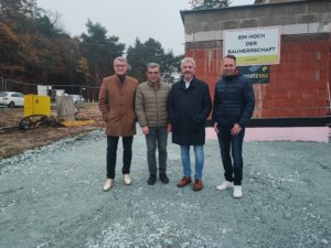 Männer an einer Baustelle vor einem Neubau mit Schild Ein Hoch der Bauherrschaft für eine örtliche Reportage von Prima Magazin.