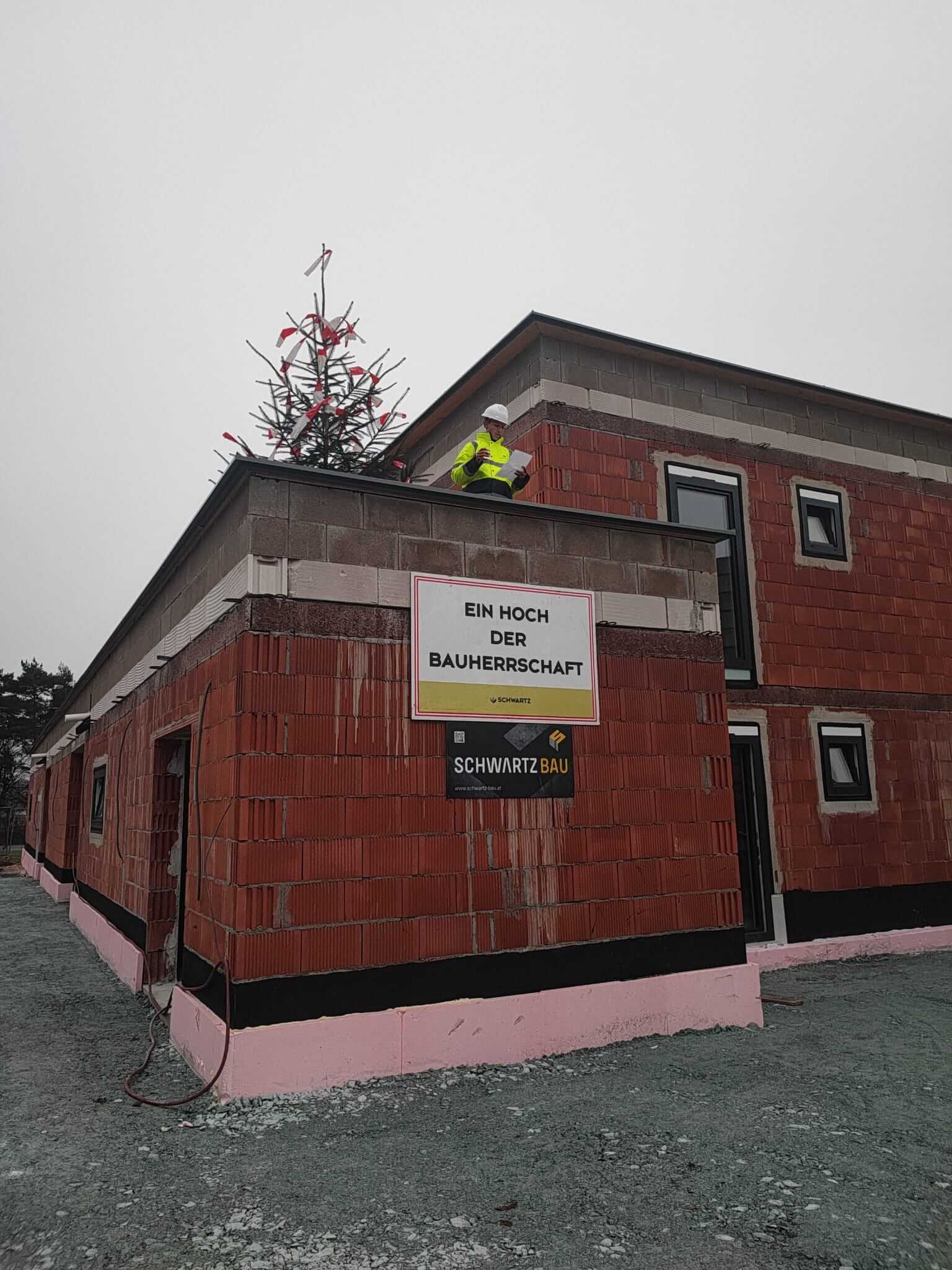 Bauarbeiter auf Rohbau mit Richtkrone bei Richtfest, Schild „Ein Hoch der Bauherrschaft“ symbolisiert erfolgreichen Baufortschritt.