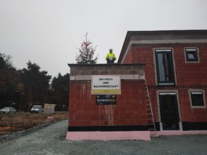 Richtfest eines Neubaus mit geschmückter Tanne; Bauleiter in Schutzkleidung auf dem Dach. Feierliche Bauphase bei Schwartz Bau.