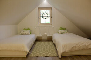 Gemütliches Dachzimmer mit zwei Einzelbetten, ruhige Atmosphäre dank sanfter Farben und dekorativen Kissen.