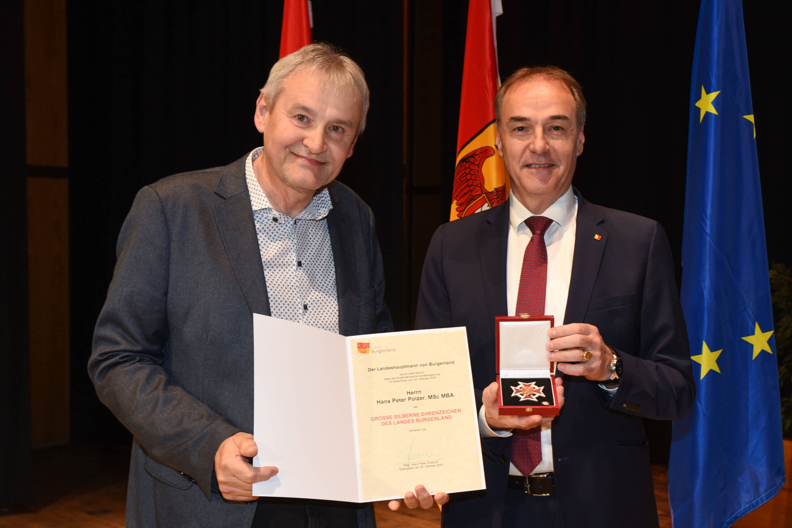 Zwei Männer bei einer Preisverleihung; einer hält Urkunde, der andere eine Auszeichnung. Symbol für Qualität und Anerkennung.