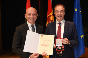 Zwei Männer bei einer Preisverleihung im Burgenland, einer hält eine Urkunde, der andere zeigt eine Auszeichnung in Schatulle.