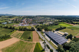 Luftaufnahme einer idyllischen Kleinstadt mit umliegenden Feldern und moderner Solaranlage unter blauem Himmel.