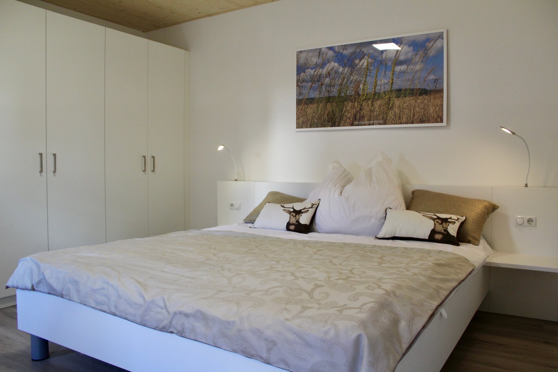 Modernes Schlafzimmer mit Doppelbett, weißen Schränken und Landschaftsbild. Gemütliche Atmosphäre für erholsamen Schlaf.