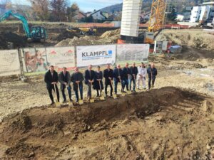 Feierlicher Spatenstich von Bauprojektteam auf einer sonnigen Baustelle, Bauarbeiter und Fachleute posieren gemeinsam.