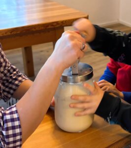 Erwachsene und Kind bereiten gemeinsam hausgemachte Butter in einem Glas zu, als Teil eines Artikels in Prima Magazin.