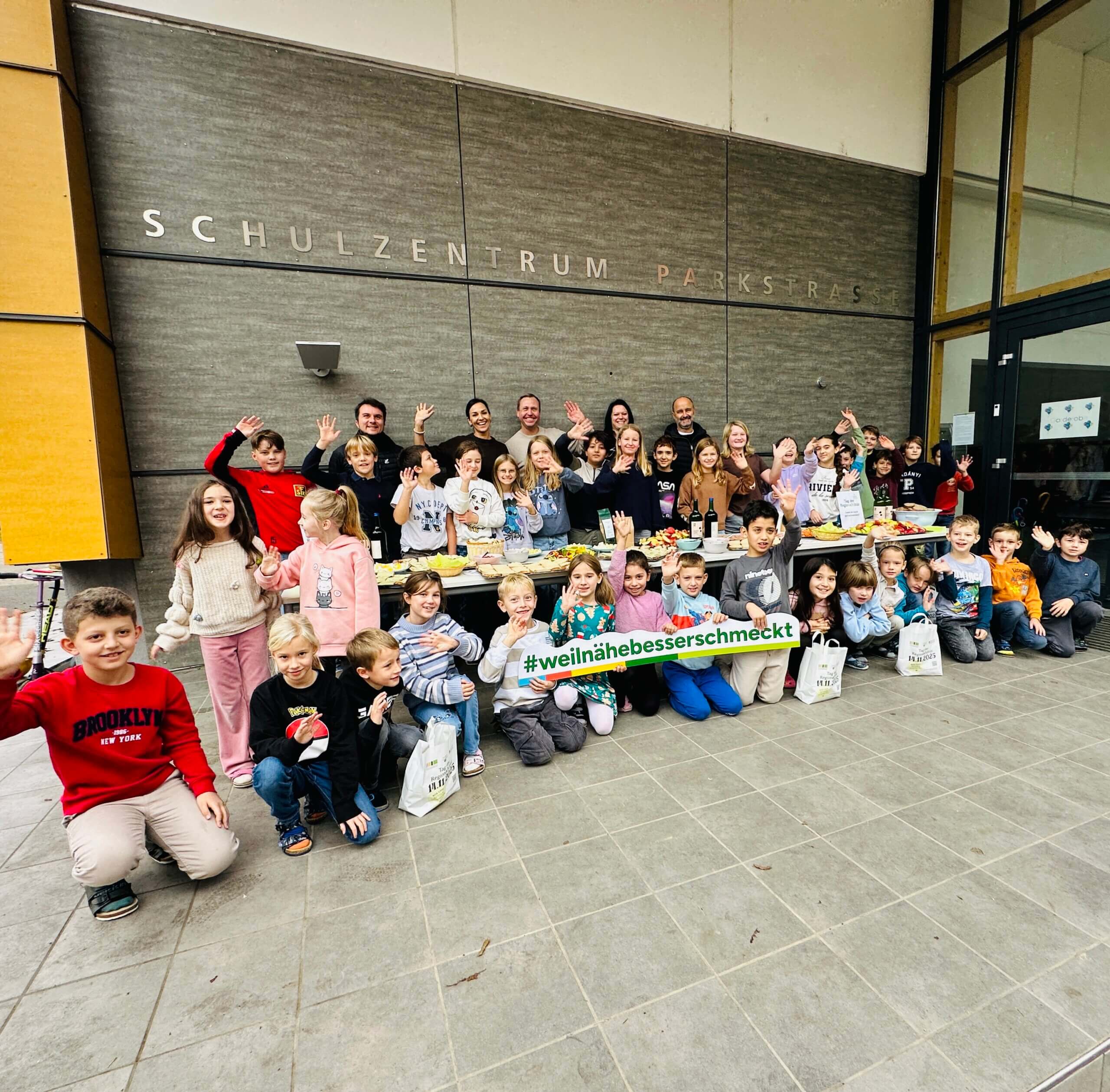 Eine fröhliche Schulkindergruppe vor dem Schulzentrum Parkstraße, die gesunde Snacks genießt, #weilnähe besserschmeckt.
