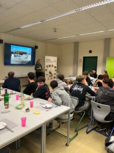 Junge Erwachsene bei einem interaktiven Vortrag in einem Klassenzimmer, fokussiert an einer Präsentation teilnehmend.