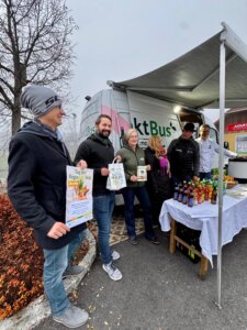 Menschen vor einem Verkaufswagen präsentieren regionale Produkte und Infomaterial beim Tag der Regionalität, unterstützt von Prima Magazin.