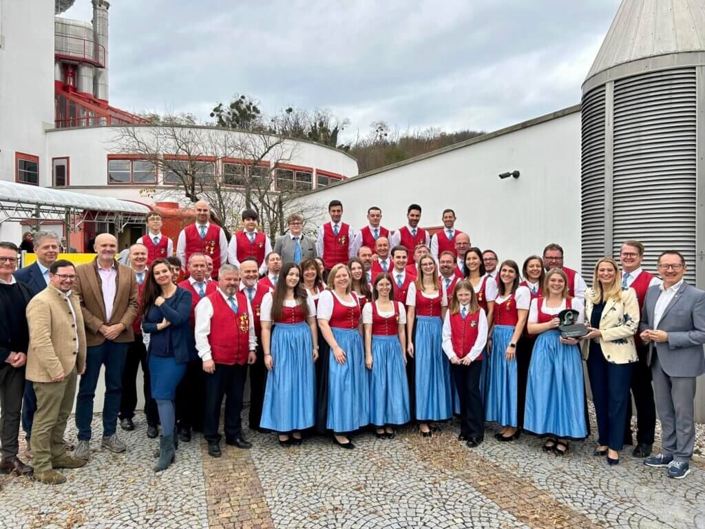 Gruppe von Menschen in traditioneller Tracht bei einer Veranstaltung vor einem modernen Gebäude, Thema: Regionales Miteinander.
