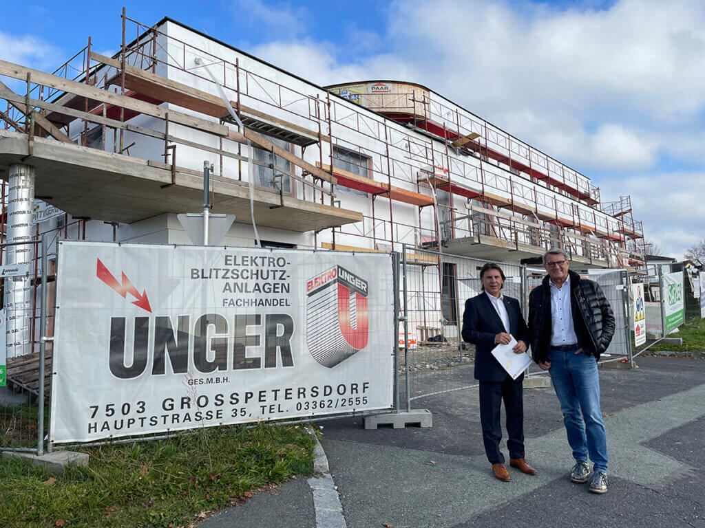 Zwei Männer vor einem im Bau befindlichen Gebäude mit Firmenschild von Elektro-Unger in Großpetersdorf, besprochen für Prima Magazin.