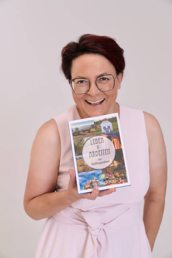 Person präsentiert Buch „Leben & Arbeiten im Südburgenland“, lächelnd in hellem Outfit - ideal für Prima Magazin-Kontext.