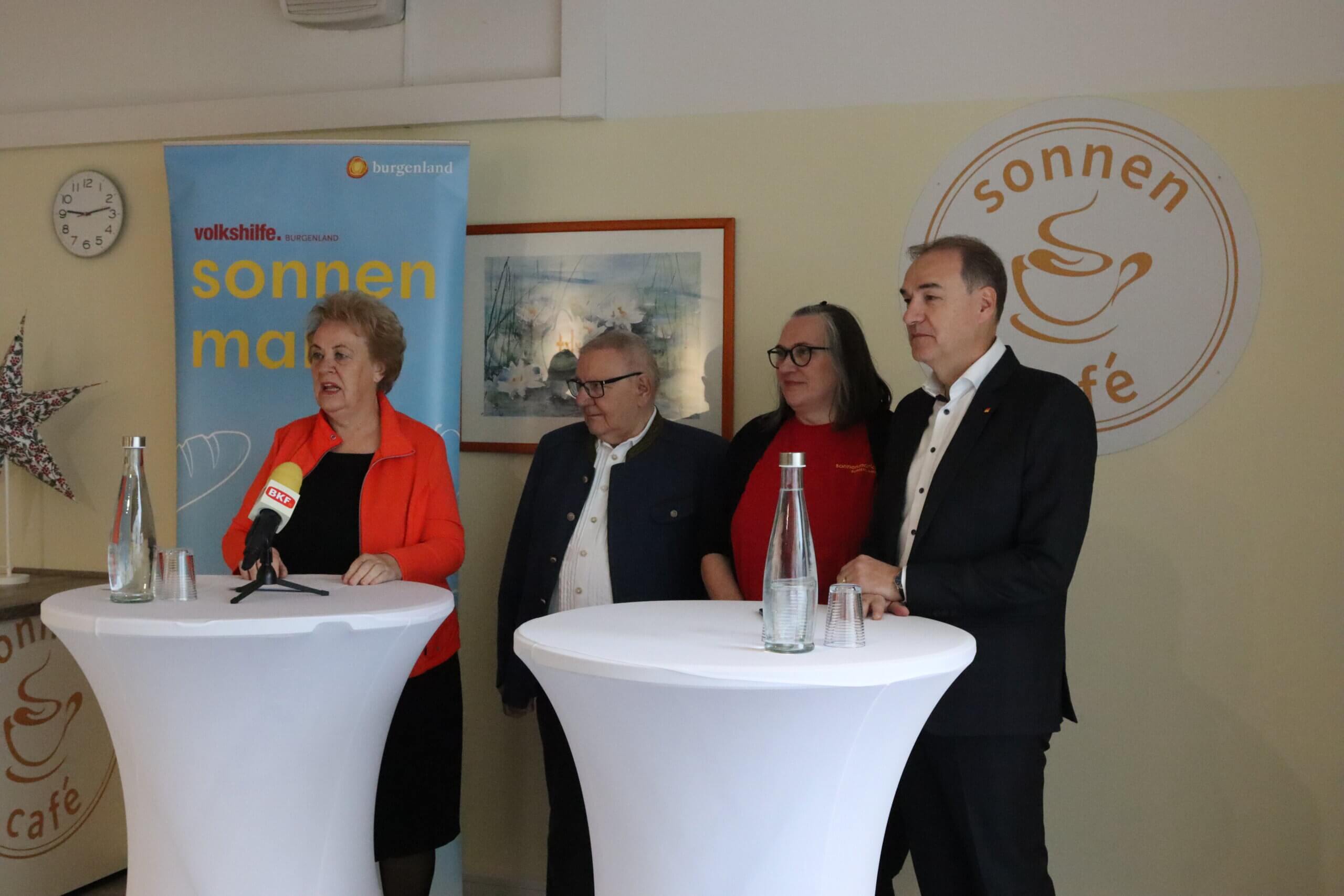 Vier Personen bei einer Pressekonferenz im Sonnencafé Burgenland, mit Mikrofonen und Logos im Hintergrund.