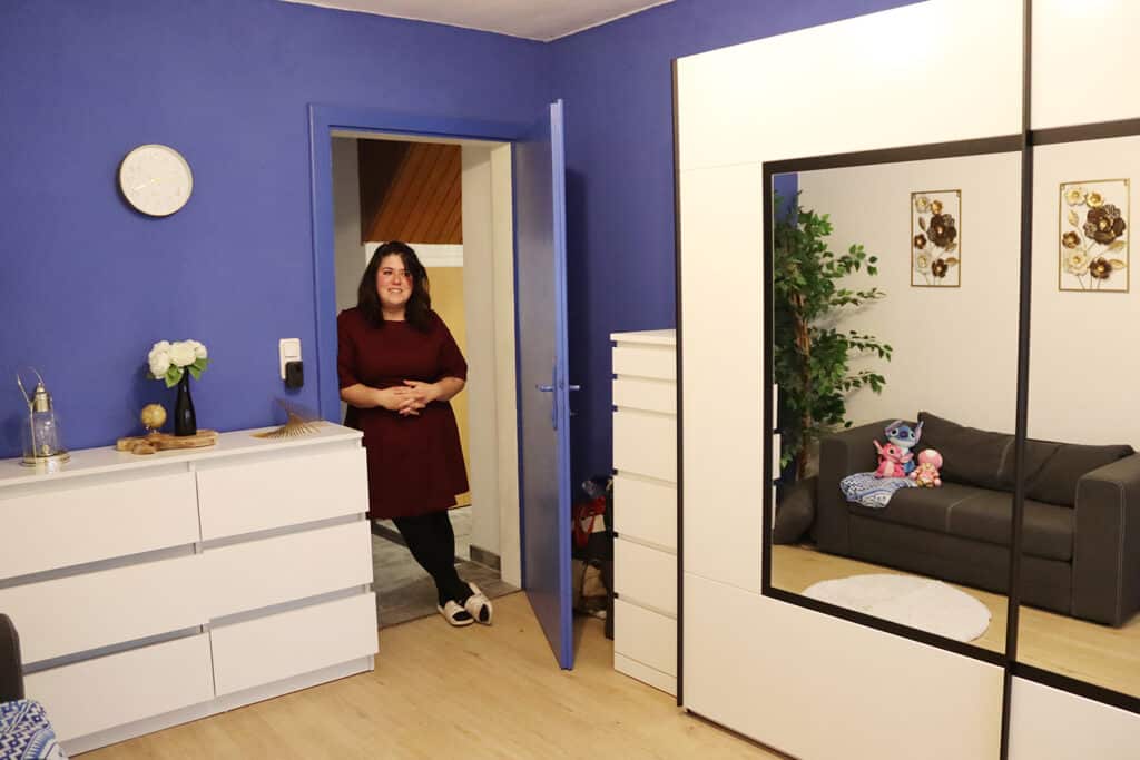Frau in einem stilvoll eingerichteten Zimmer mit blauer Wand, weißen Möbeln und gemütlicher Atmosphäre, passend zum Thema Wohntrends.