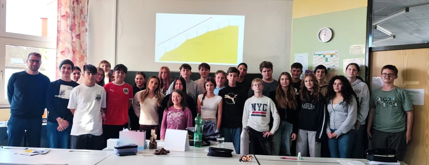 Gruppe von Schülern und Lehrern in einem Klassenzimmer vor einer Projektionsleinwand.