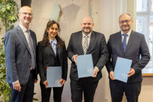 Vier Personen in Businesskleidung präsentieren Dokumente in einem Büro. Event für qualitätsorientierten Regionaljournalismus.