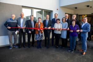 Gruppe von Menschen durchschneidet feierlich ein rotes Band vor einem neuen Gebäude, als Teil einer Eröffnung.