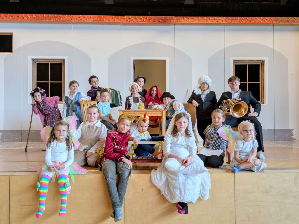 Kinder in Kostümen führen ein Theaterstück auf einer Bühne auf, beleuchtet von einem gemütlichen, lokalen Ambiente.