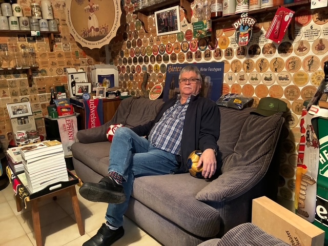 Mann entspannt in rustikalem Raum voller Bierdeckel und Sammlerstücke—Perfekte Szene für regionales Reportage-Thema im Prima Magazin.