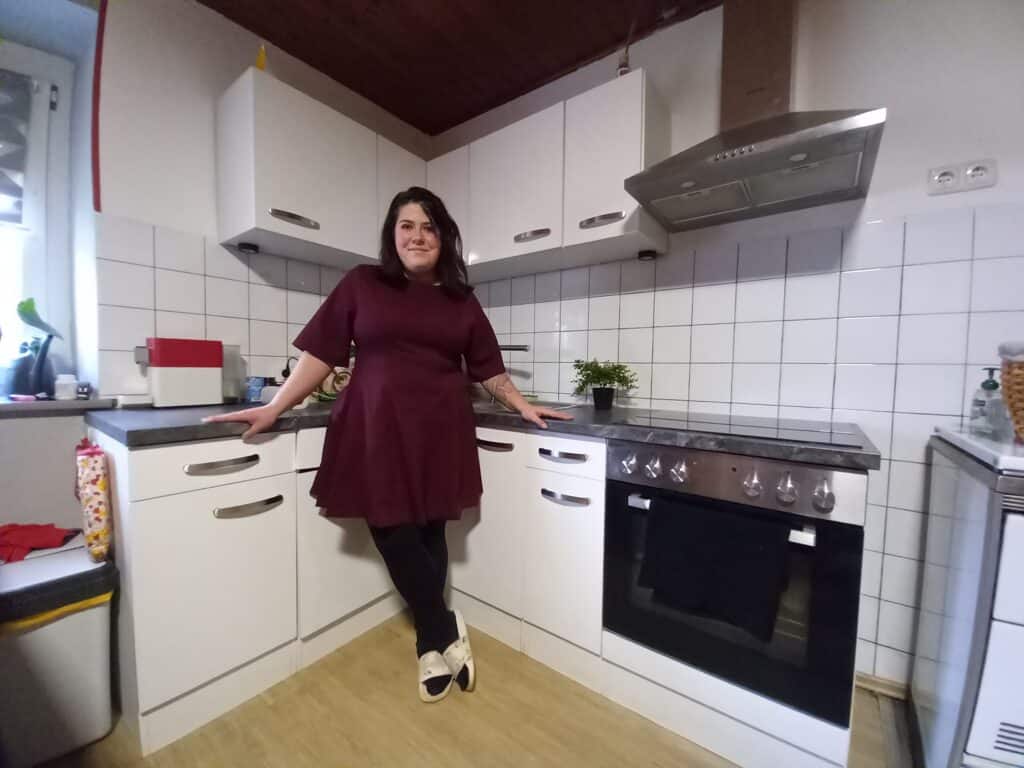 Frau in moderner Küche lehnt lächelnd am Schrank, vermittelt heimische Gemütlichkeit. Ideal für Prima Magazin Artikel.