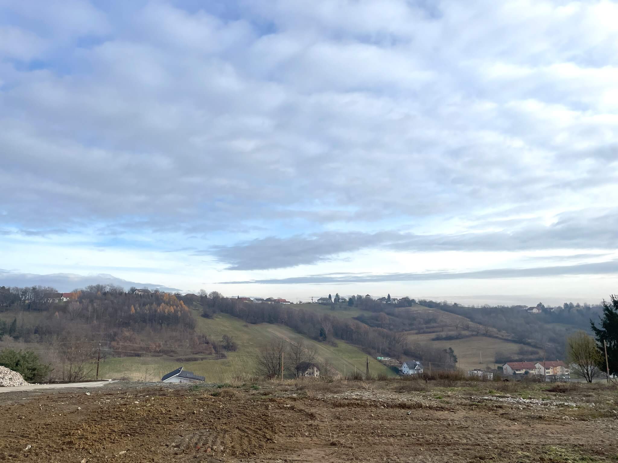Hügelige Landschaft mit verstreuten Häusern und bewölktem Himmel, ideal für Artikel im regionalen Magazin Prima.