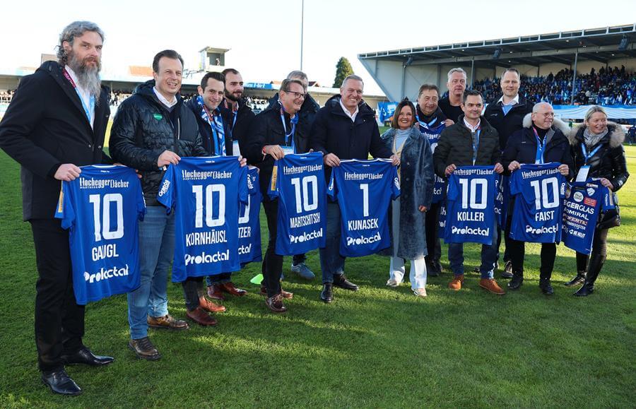 Gruppe von Menschen auf einem Fußballplatz, die personalisierte Trikots halten und lächeln, geeignet für Prima Magazin.