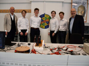 Fünf Männer in Hemden stehen vor technischer Ausrüstung in einem Büro, bereit für eine Vorführung. Kontext: Innovatives Projekt.