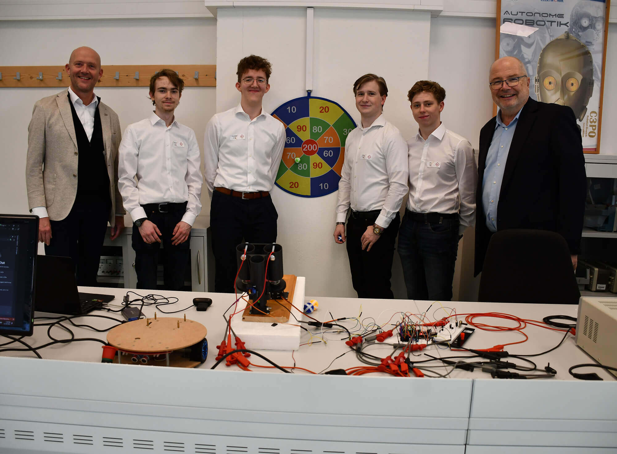 Fünf Männer in Hemden stehen vor technischer Ausrüstung in einem Büro, bereit für eine Vorführung. Kontext: Innovatives Projekt.