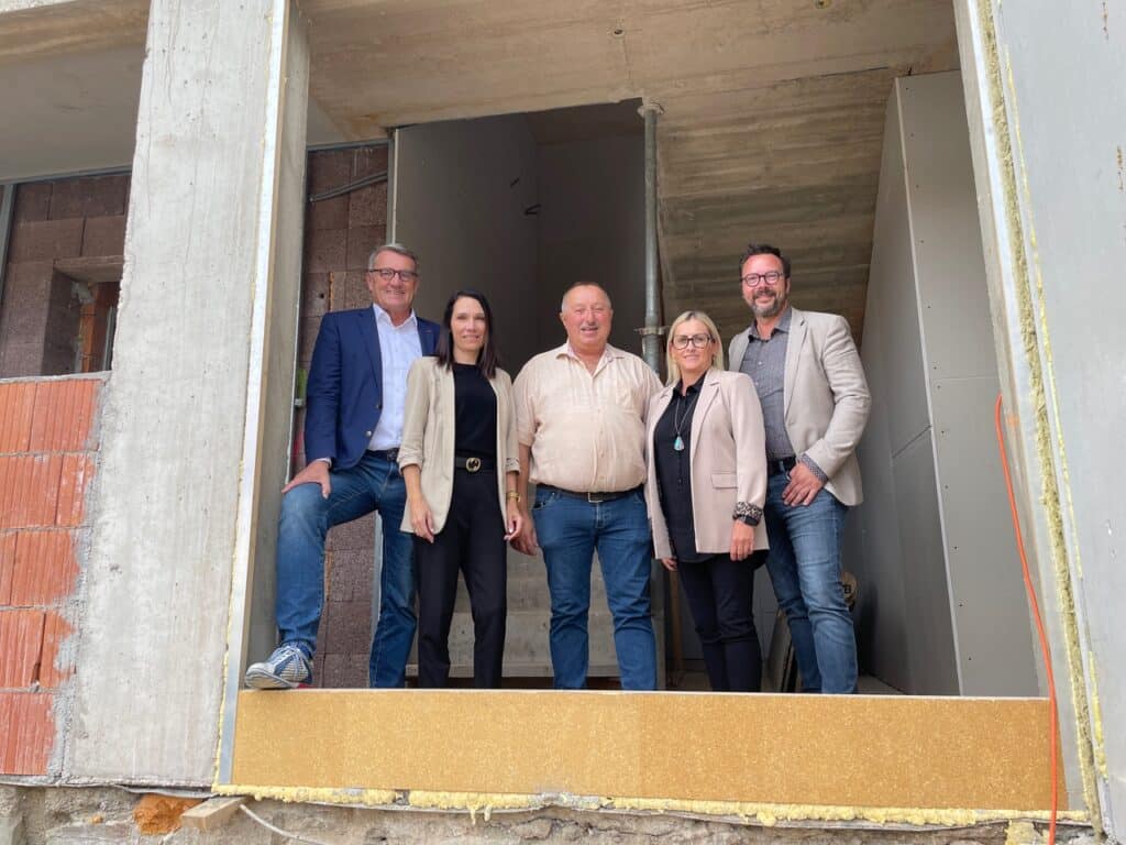 Eine Gruppe von fünf Personen steht lächelnd in einem Rohbau und zeigt Teamgeist bei einem Bauprojekt für Prima Magazin.