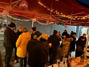 Belebtes Winterfest in gemütlicher Atmosphäre mit Menschen in warmer Kleidung unter einem festlich geschmückten Pavillon.
