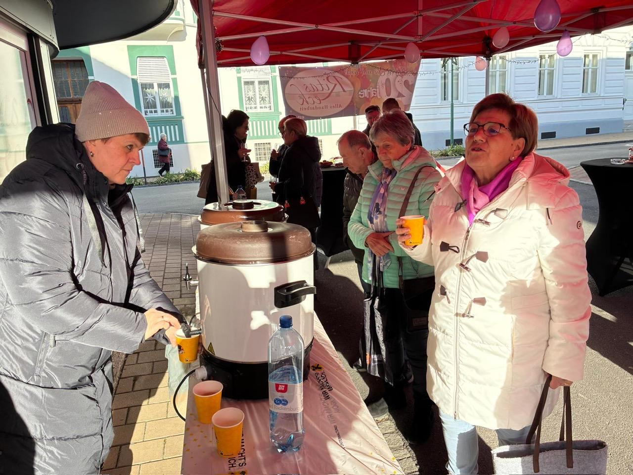 Personen genießen heißen Punsch bei einem regionalen Event unter einem roten Pavillon; Prima Magazin berichtet.