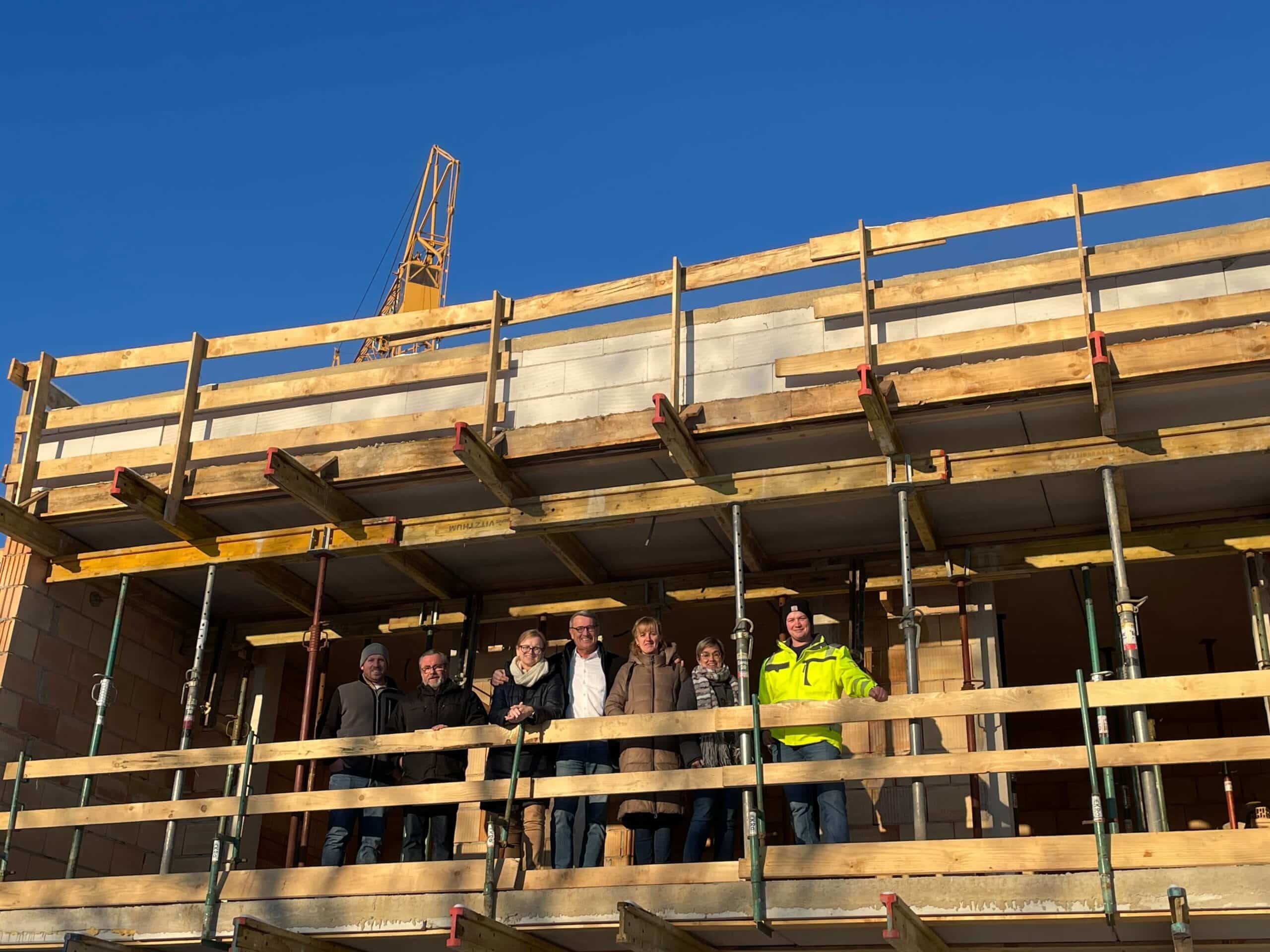 Gruppe Menschen auf Baustelle vor Rohbau, blauer Himmel; Symbol für Wachstum und Gemeinschaft im regionalen Journalismus.
