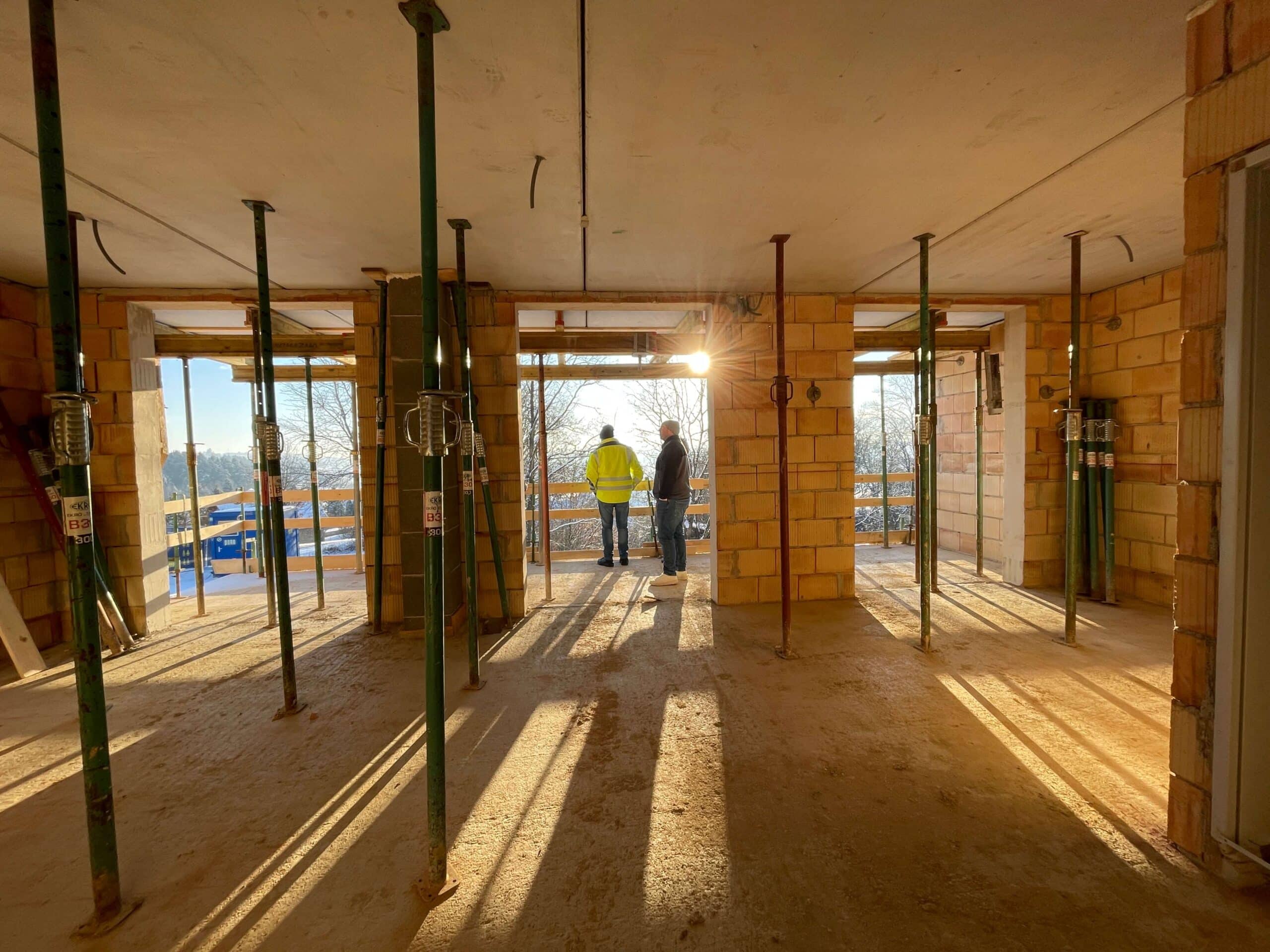 Bauleiter begutachten bei Sonnenuntergang die Baustelle eines Rohbaus, symbolisch für Fortschritt im regionalen Wohnungsbau.