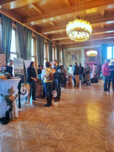 Besucher erkunden Stände auf einer regionalen Messe in festlich dekoriertem Saal, beleuchtet von großen Kronleuchtern.