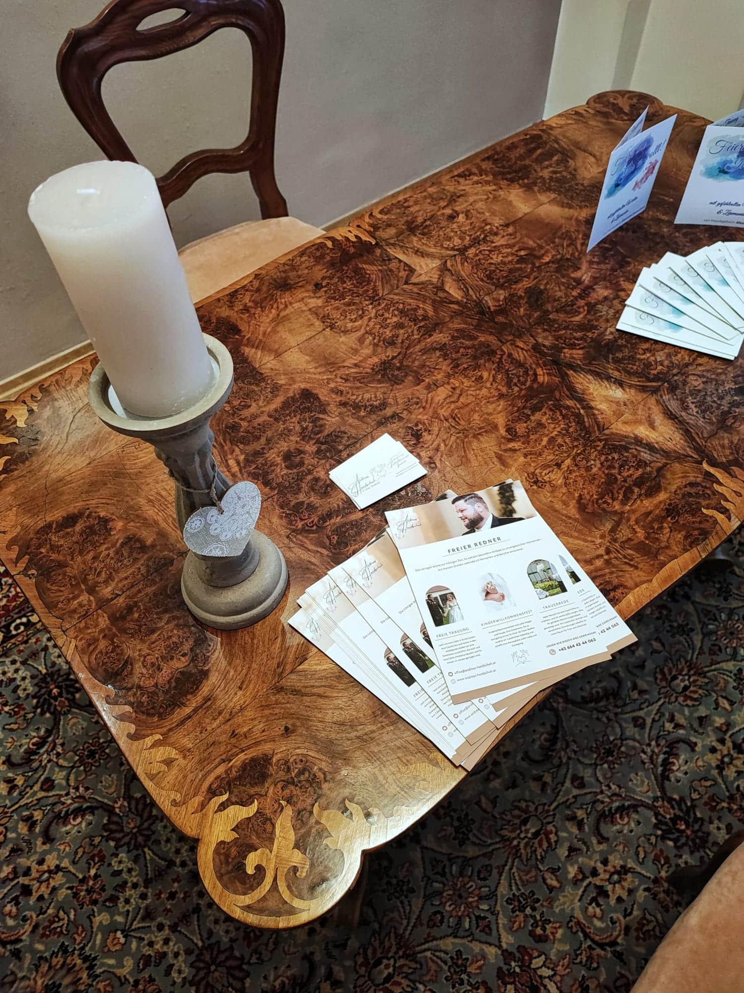 Flyer und Visitenkarten auf einem eleganten Holztisch mit Kerze, vermitteln Informationen und laden zum Entdecken auf Prima Magazin ein.