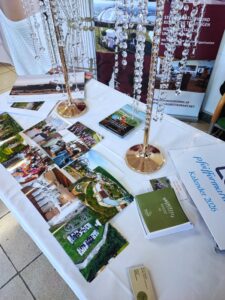 Tisch mit Fotos und Broschüren zu regionalen Veranstaltungen, dekoriert mit eleganten Kristallketten für eine Messe.