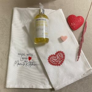 Geschirrtücher mit Herzmotiv, Spülmittel und Herzdeko auf Tisch. Perfekt für regionale Küche, wie im Prima Magazin gezeigt.