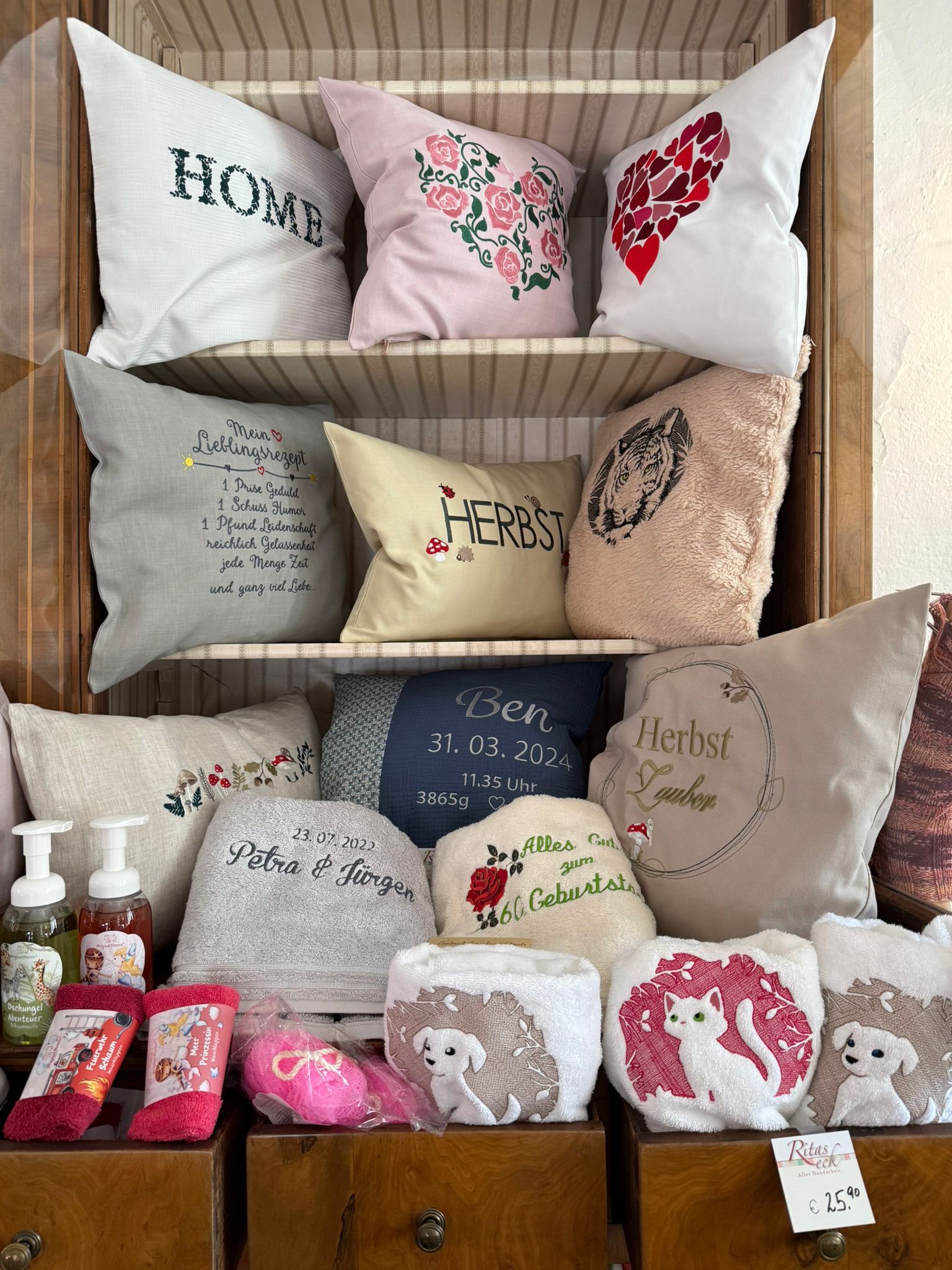 Kissen mit personalisierten Stickereien und Handtüchern in einem Regal, ideal für individuelle Geschenke und kreative Wohnideen.