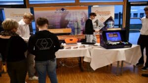 Besucher auf einer Messe am Stand von HTL Pinkafeld, umgeben von Informatik-Bannern und einem Retro-Arcade-Spiel.