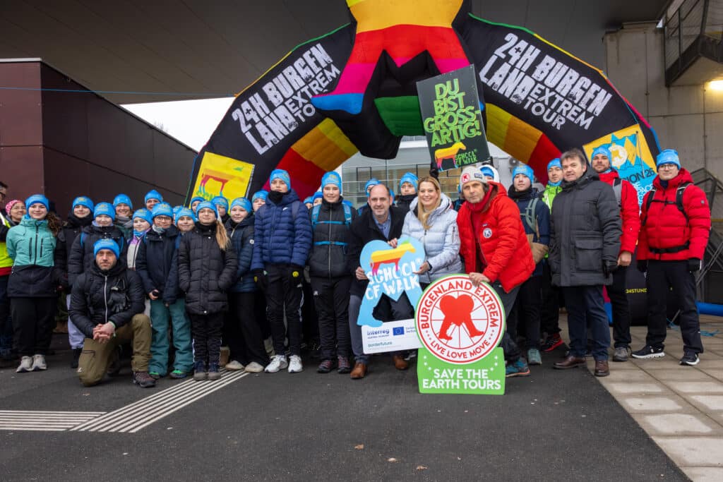 Gruppe von Teilnehmern der 24h Burgenland Extrem Tour in Outdoor-Kleidung mit Bannern für Umweltschutz und Gemeinschaft. Bildungslandesrätin Daniela Winkler beim Start von „School of Walk“ in Neusiedl am See