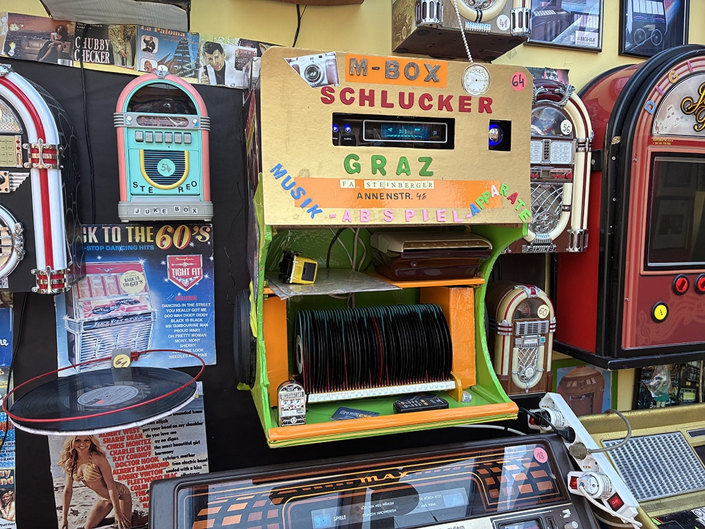Bunte Jukebox-Ausstellung in Graz; Vintage Musikautomaten und Poster aus den 60ern, nostalgisches Flair im regionalen Fokus.