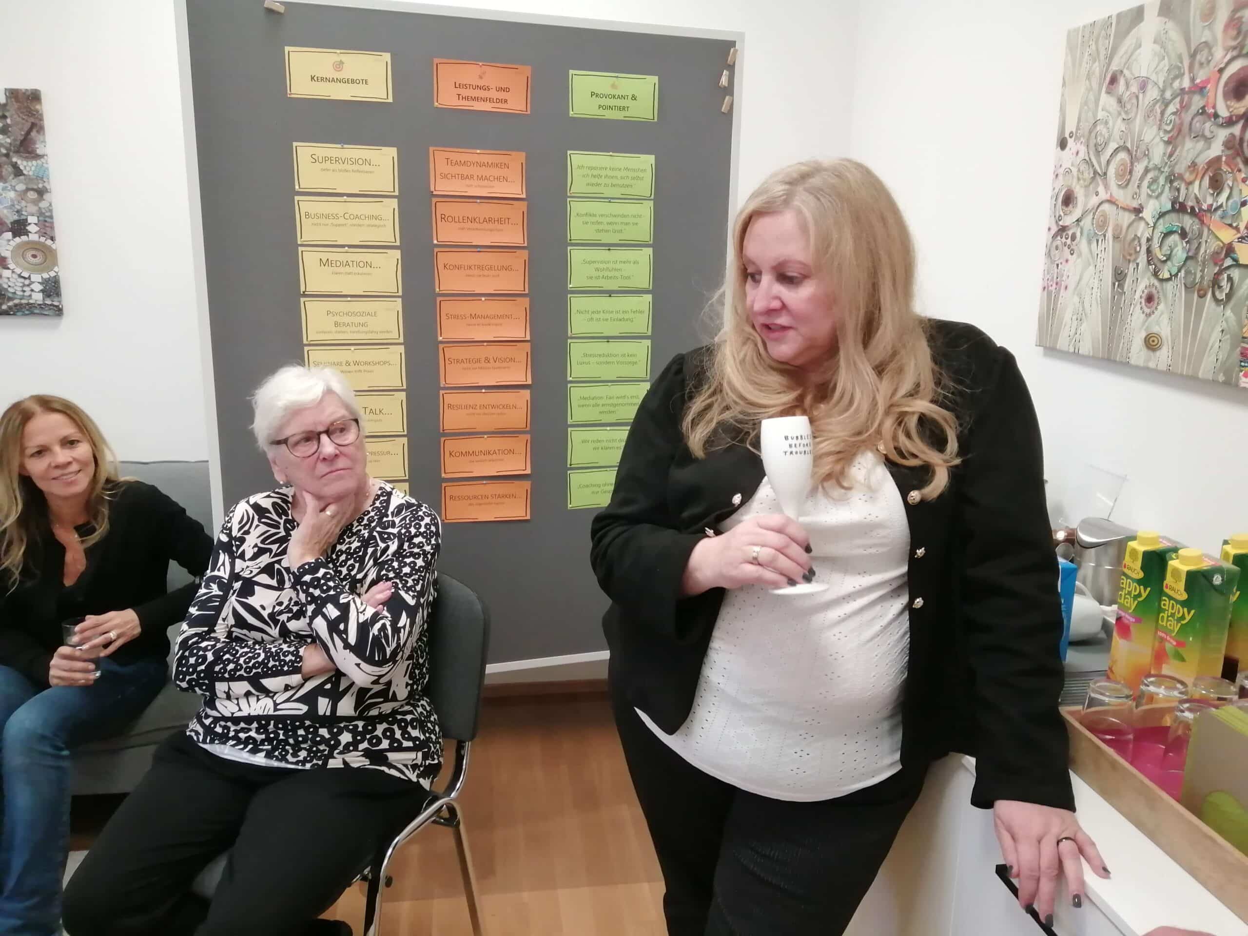 Frauen im Gespräch bei Büroevent, umgeben von Teaminformationsplakaten. Prima Magazin bietet Qualitätsjournalismus und regionale Themen.